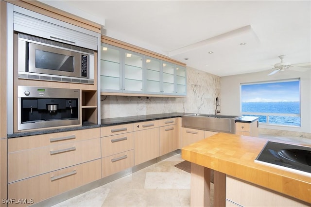 kitchen featuring stainless steel microwave, sink, ceiling fan, decorative backsplash, and light brown cabinetry