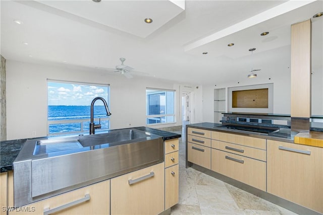 kitchen with ceiling fan, a water view, light brown cabinetry, and black cooktop