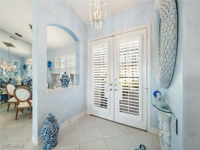 foyer entrance with french doors, light tile patterned floors, vaulted ceiling, and an inviting chandelier