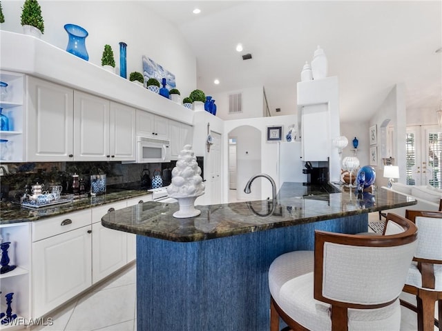 kitchen with kitchen peninsula, white cabinets, dark stone counters, and light tile patterned floors