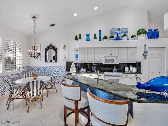 kitchen featuring dark stone counters, white appliances, vaulted ceiling, white cabinets, and hanging light fixtures