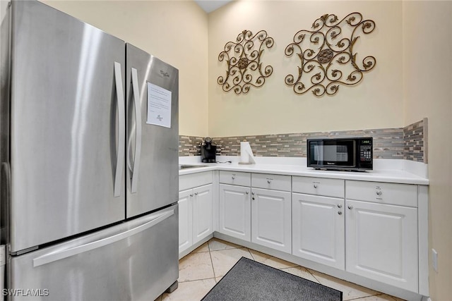 kitchen featuring stainless steel refrigerator, white cabinetry, light tile patterned floors, and decorative backsplash