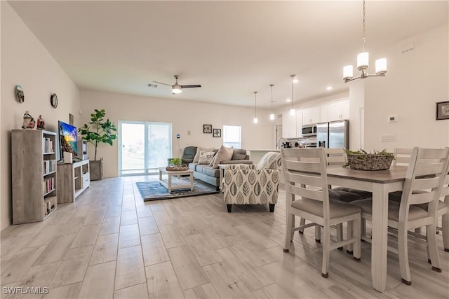 dining area with light wood-style floors and ceiling fan with notable chandelier