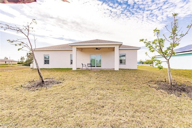 rear view of house with stucco siding, ceiling fan, and a yard