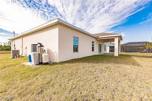 rear view of house with ceiling fan, central AC, a lawn, and stucco siding