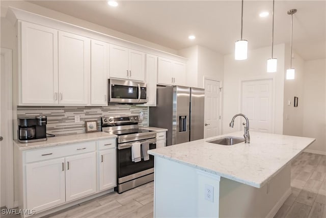 kitchen featuring white cabinetry, sink, stainless steel appliances, decorative light fixtures, and a center island with sink