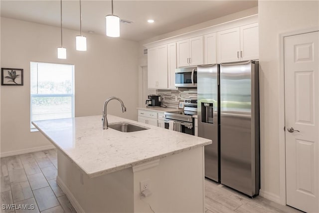 kitchen featuring appliances with stainless steel finishes, sink, a center island with sink, white cabinetry, and hanging light fixtures