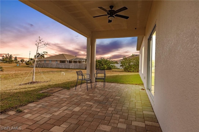 patio terrace at dusk featuring a yard and a ceiling fan