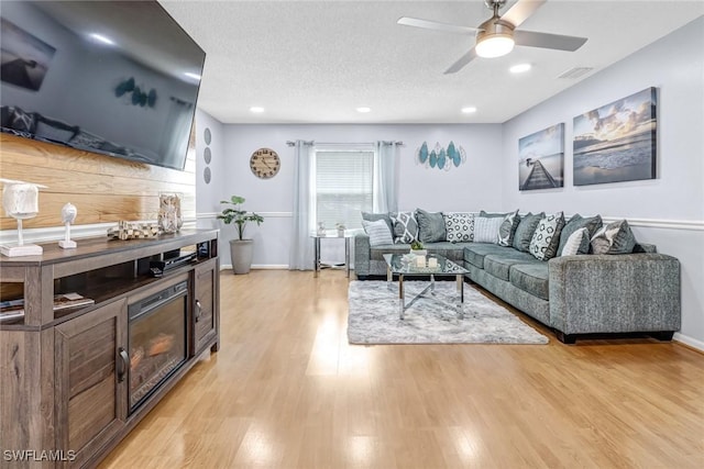 living room with a textured ceiling, light wood-type flooring, and ceiling fan