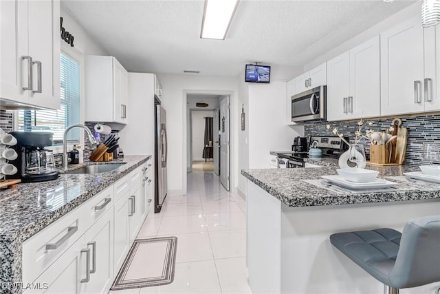 kitchen featuring decorative backsplash, stainless steel appliances, sink, stone counters, and white cabinets