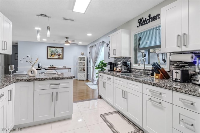 kitchen featuring dark stone counters, sink, ceiling fan, decorative light fixtures, and white cabinetry