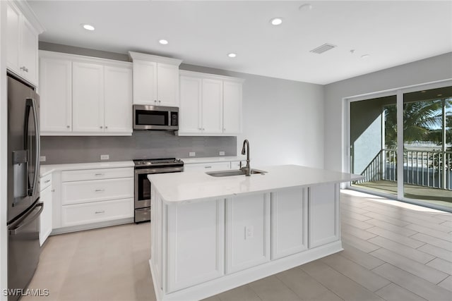 kitchen featuring sink, backsplash, a center island with sink, white cabinets, and appliances with stainless steel finishes