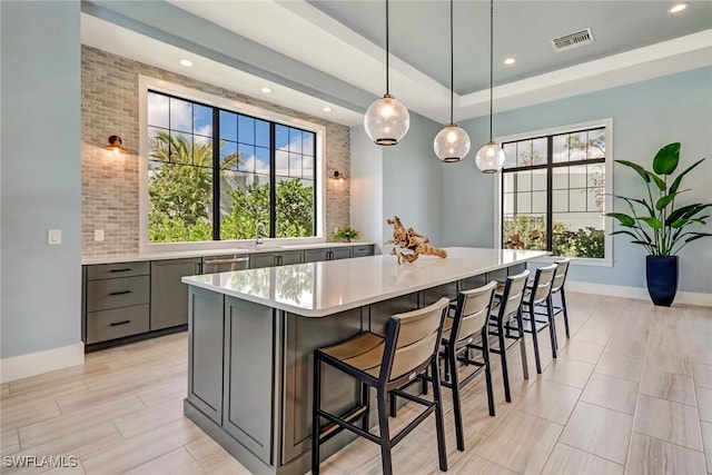 kitchen with gray cabinetry, a large island, stainless steel dishwasher, decorative light fixtures, and a breakfast bar area