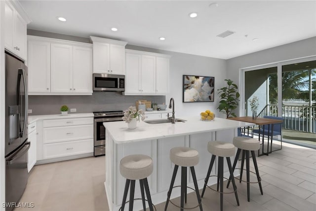 kitchen with a kitchen island with sink, sink, appliances with stainless steel finishes, a kitchen bar, and white cabinetry