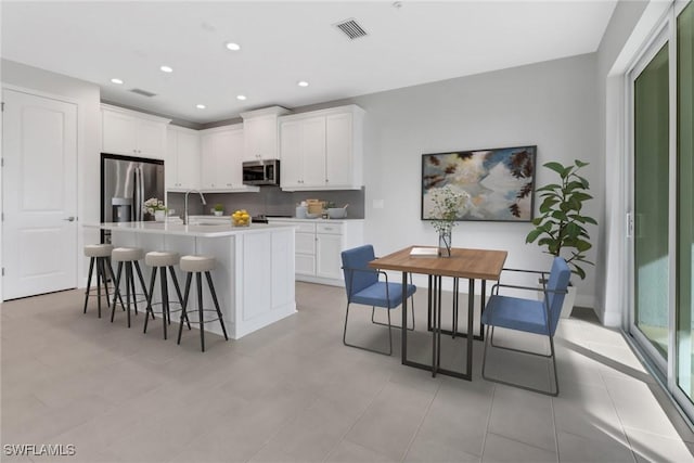 kitchen with white cabinets, appliances with stainless steel finishes, a center island with sink, and a kitchen breakfast bar