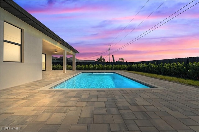 pool at dusk with a patio and ceiling fan