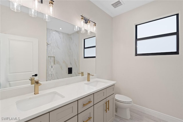 bathroom with tiled shower, vanity, and toilet