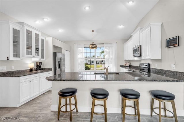kitchen with glass insert cabinets, white cabinets, a peninsula, dark stone counters, and stainless steel appliances