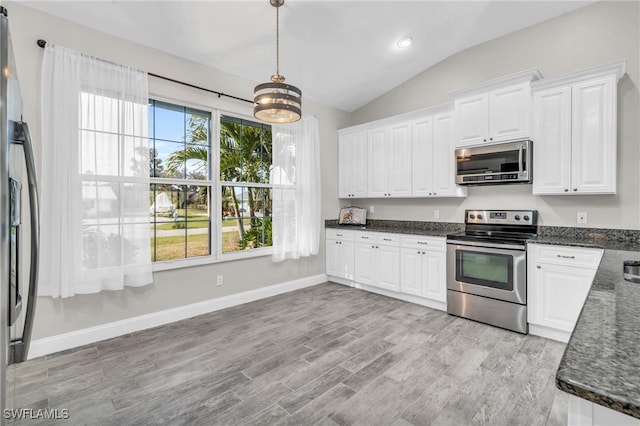 kitchen featuring dark stone counters, vaulted ceiling, appliances with stainless steel finishes, light wood-style floors, and white cabinetry