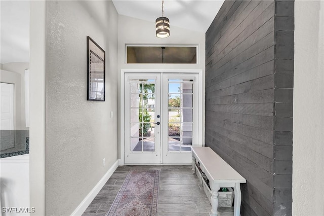 interior space featuring baseboards, a textured wall, vaulted ceiling, wood finished floors, and french doors