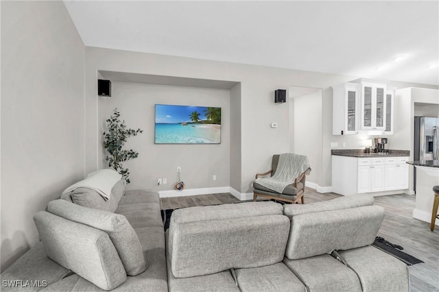 living area featuring light wood-style flooring, wet bar, and baseboards