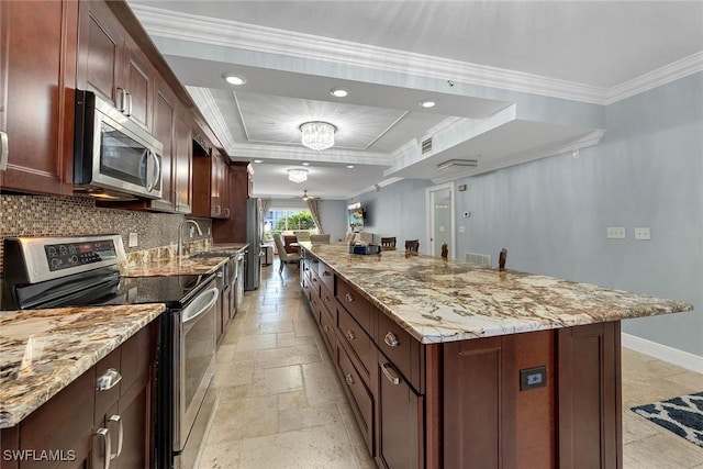 kitchen with a tray ceiling, a kitchen island, ornamental molding, and appliances with stainless steel finishes