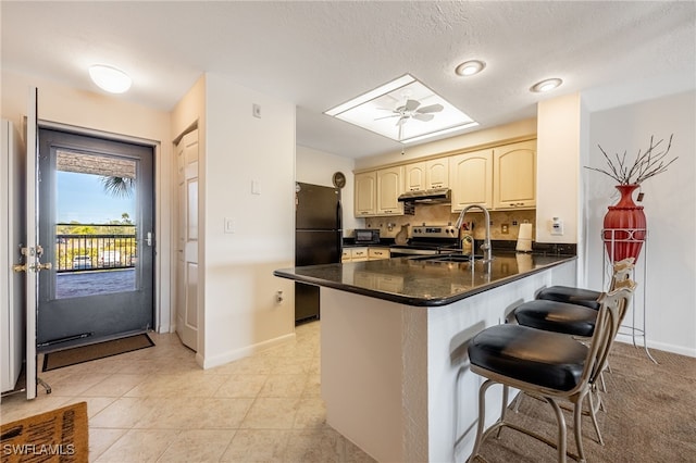 kitchen with freestanding refrigerator, a peninsula, stainless steel electric stove, under cabinet range hood, and a sink