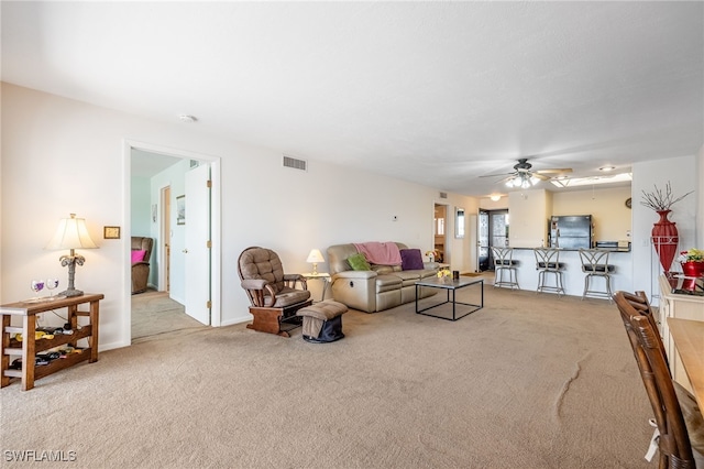 living area with light carpet, ceiling fan, visible vents, and baseboards