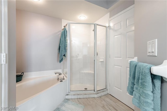 full bathroom featuring a bath, a stall shower, and wood finished floors