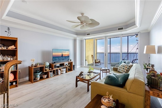 living room with light wood-type flooring, a tray ceiling, ceiling fan, and ornamental molding