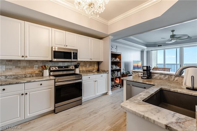 kitchen featuring white cabinetry, ornamental molding, stainless steel appliances, a sink, and light stone counters