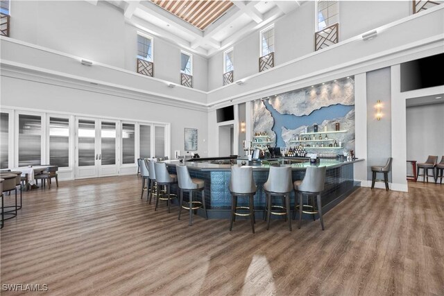 bar with beamed ceiling, a healthy amount of sunlight, wood-type flooring, and a towering ceiling