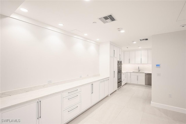 kitchen featuring sink, light tile patterned floors, dishwasher, white cabinetry, and decorative backsplash