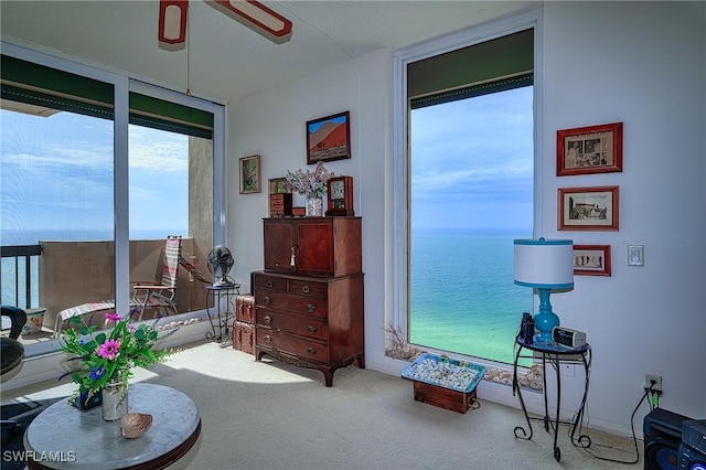 living area with ceiling fan, a water view, carpet flooring, and a wall of windows