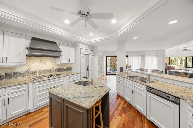 kitchen featuring white cabinetry, custom range hood, stainless steel appliances, and an island with sink