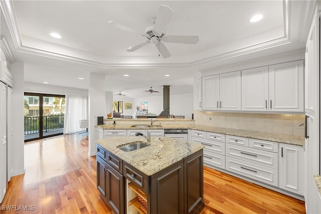 kitchen with a tray ceiling, kitchen peninsula, white cabinetry, and sink