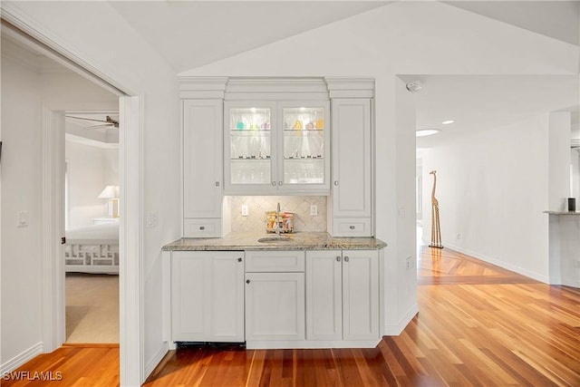 bar with backsplash, white cabinetry, ceiling fan, and vaulted ceiling