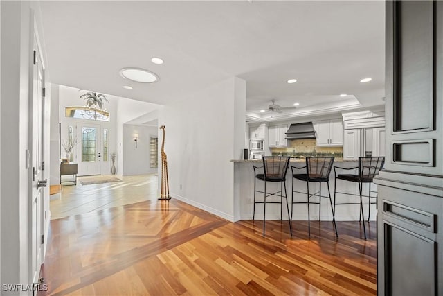 kitchen with wall chimney range hood, a kitchen breakfast bar, kitchen peninsula, a tray ceiling, and white cabinets