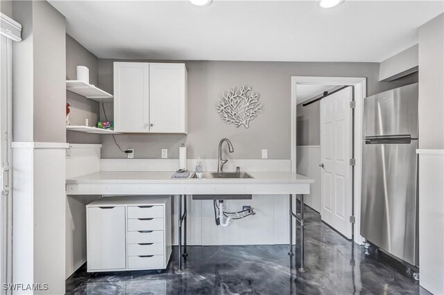 kitchen with white cabinets, stainless steel fridge, a barn door, and sink