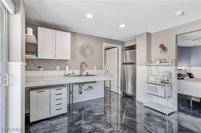 kitchen featuring kitchen peninsula, white cabinetry, stainless steel refrigerator, a kitchen breakfast bar, and sink