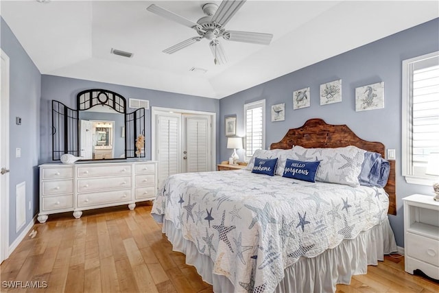 bedroom featuring lofted ceiling, ceiling fan, a tray ceiling, light wood-type flooring, and a closet