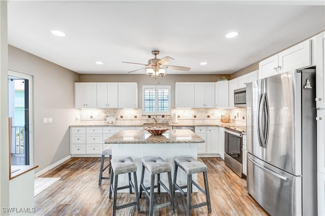 kitchen with stainless steel appliances, a kitchen bar, a kitchen island, and white cabinets