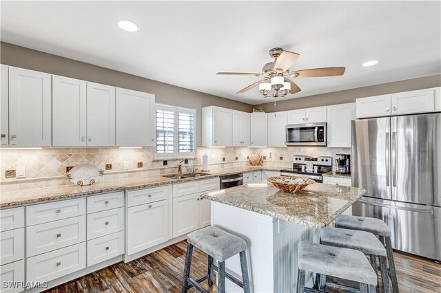 kitchen with sink, white cabinets, light stone countertops, a breakfast bar, and appliances with stainless steel finishes