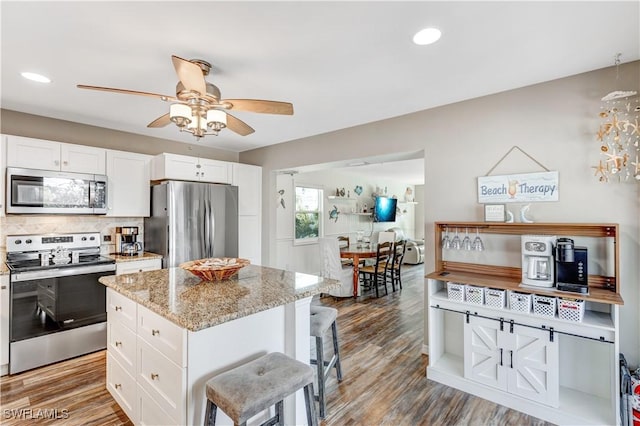 kitchen with a kitchen island, a breakfast bar area, white cabinets, light stone counters, and stainless steel appliances