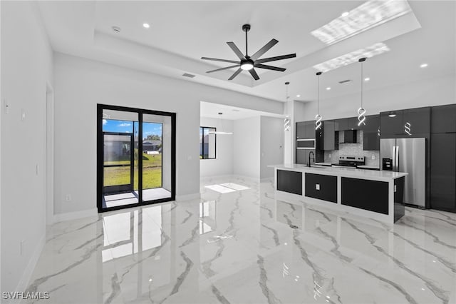 kitchen with ceiling fan, stainless steel appliances, backsplash, decorative light fixtures, and a kitchen island with sink