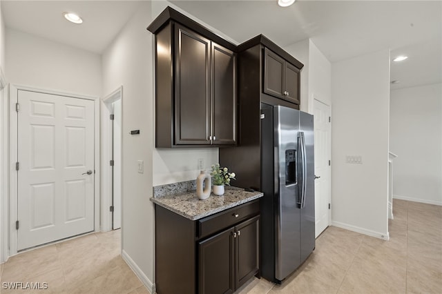 kitchen featuring light stone counters, stainless steel fridge with ice dispenser, dark brown cabinets, and light tile patterned floors