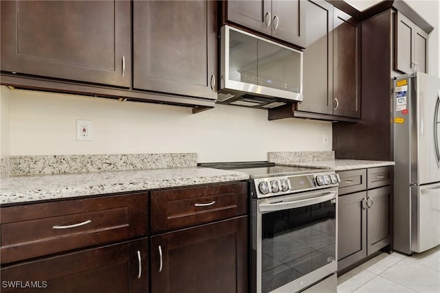 kitchen with light tile patterned flooring, dark brown cabinetry, light stone countertops, and stainless steel appliances