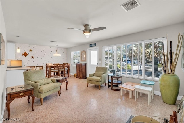 living area featuring light speckled floor, a ceiling fan, baseboards, visible vents, and wallpapered walls