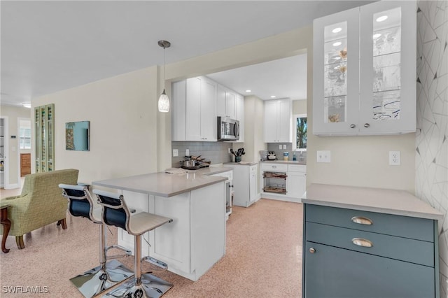 kitchen featuring light countertops, white cabinets, stainless steel microwave, and decorative light fixtures