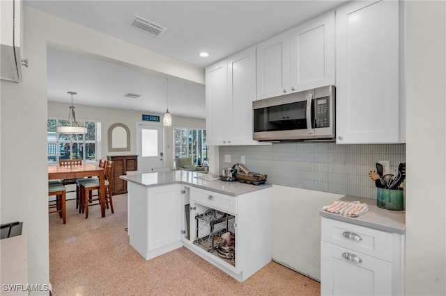 kitchen featuring light countertops, white cabinets, stainless steel microwave, and visible vents